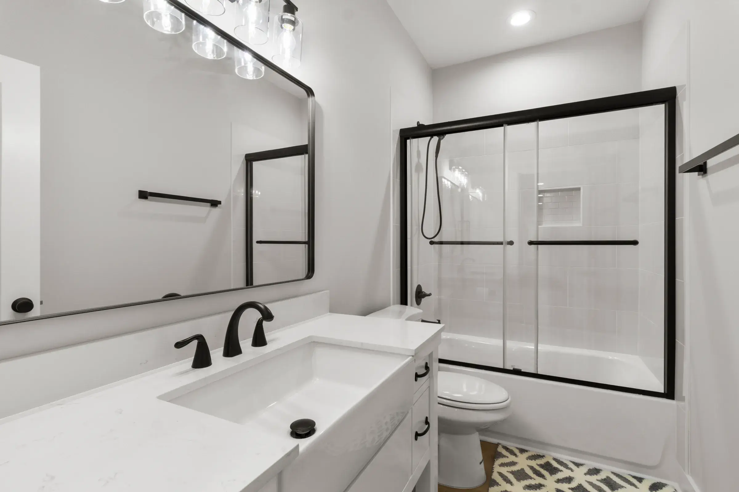 Bathroom with a white vanity, black faucet, large mirror, and a tub shower with sliding glass doors.