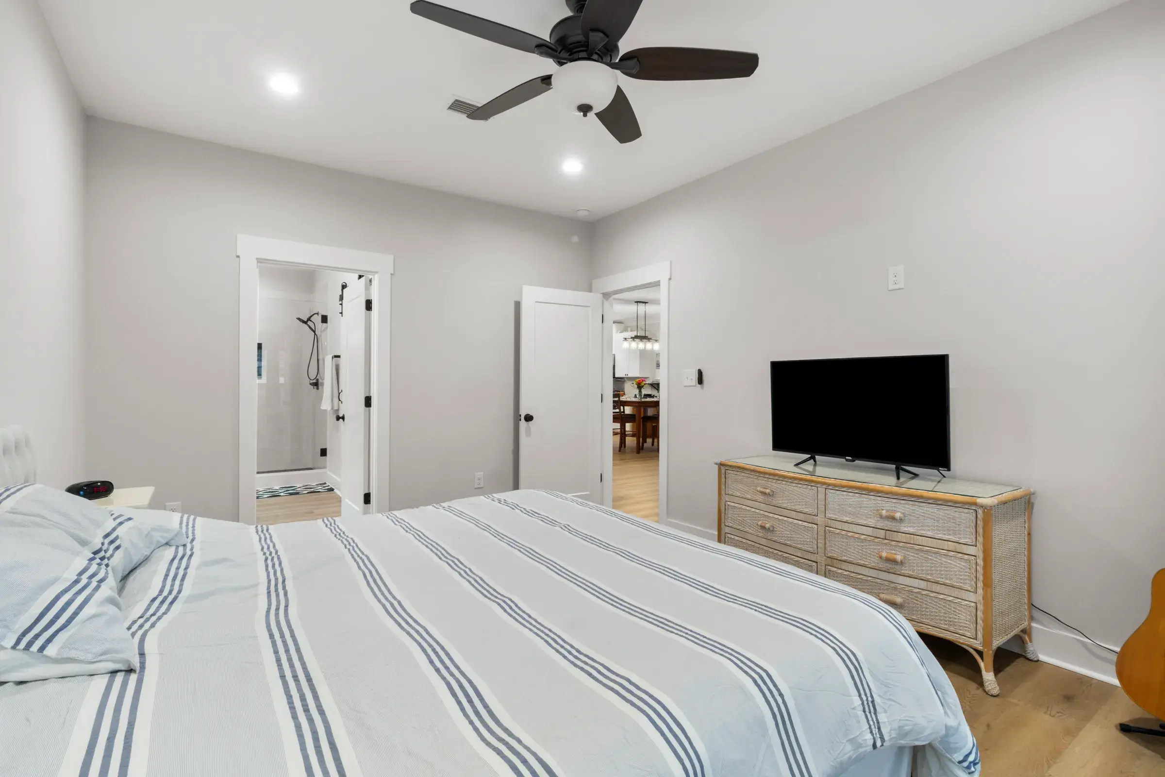 Furnished bedroom with a dresser and TV and an open door to the en suite bathroom.