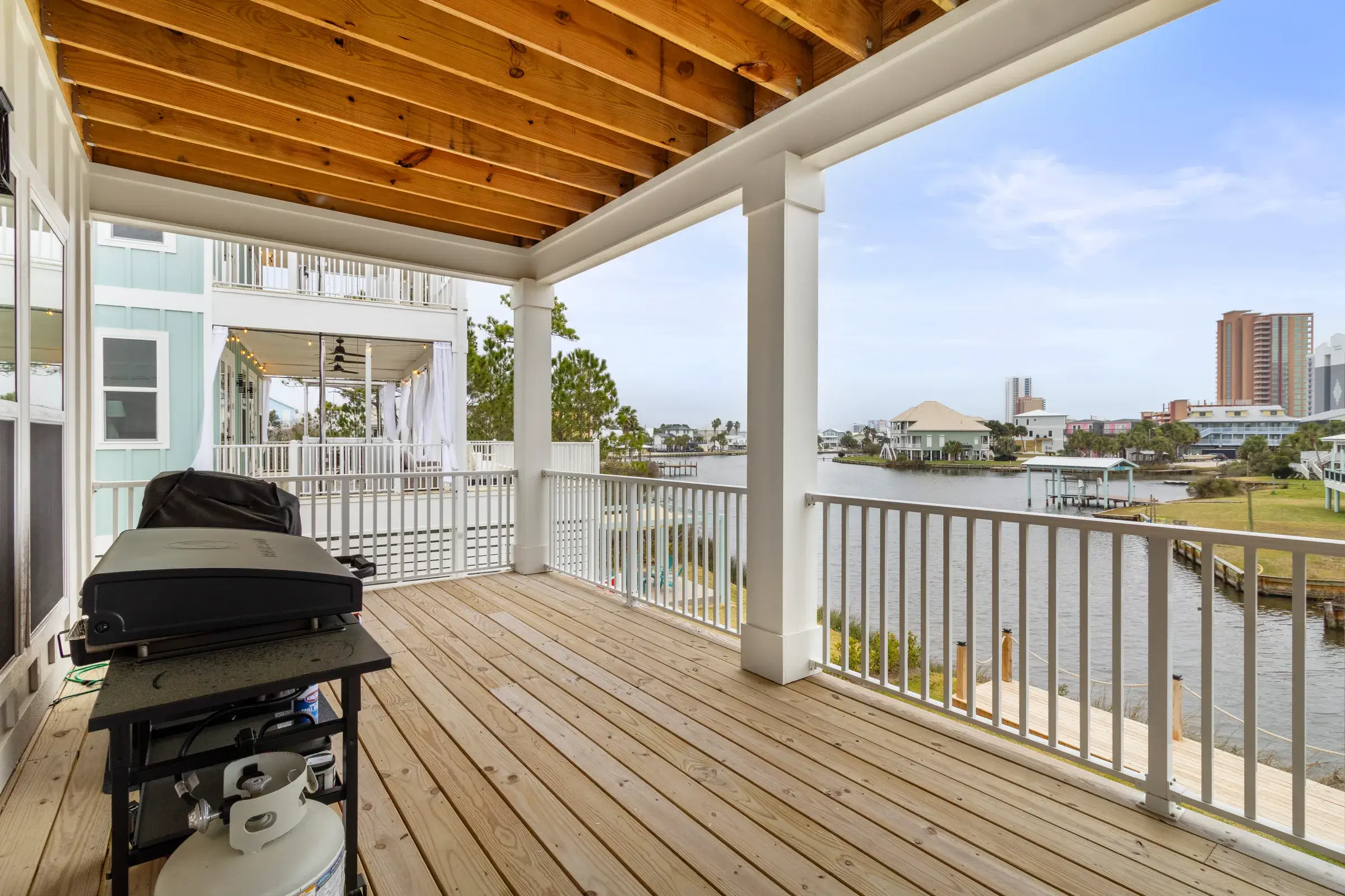 Covered wood deck with a gas grill, white railings and a view over the lagoon.