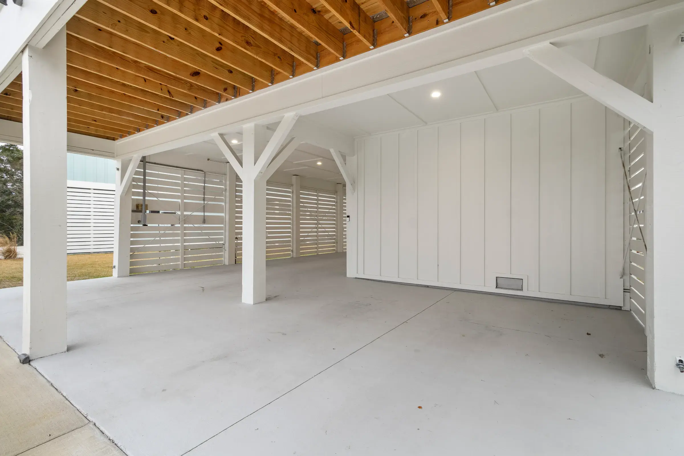 Concrete parking bay beneath the house with white board-and-batten walls, support posts and slatted screens.