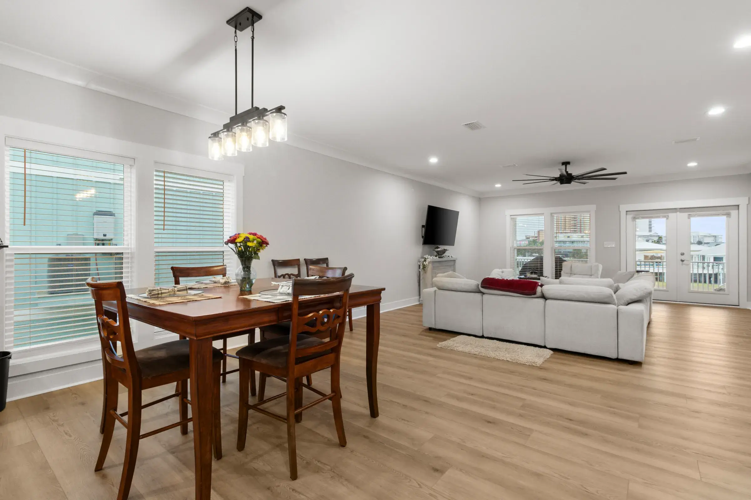 Wood dining table in front of a bright open living room with a sectional sofa and French doors.