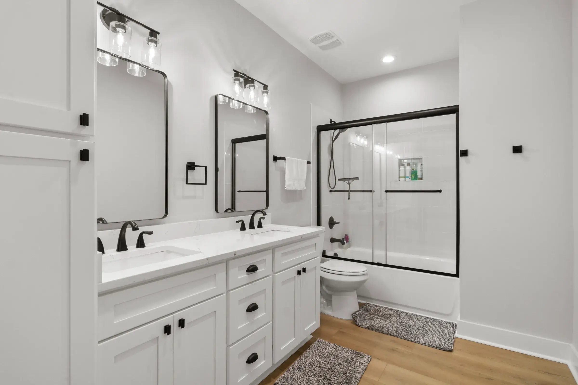 Bathroom with white double vanity, black fixtures, framed mirrors, and a tub shower behind a black-framed glass door.