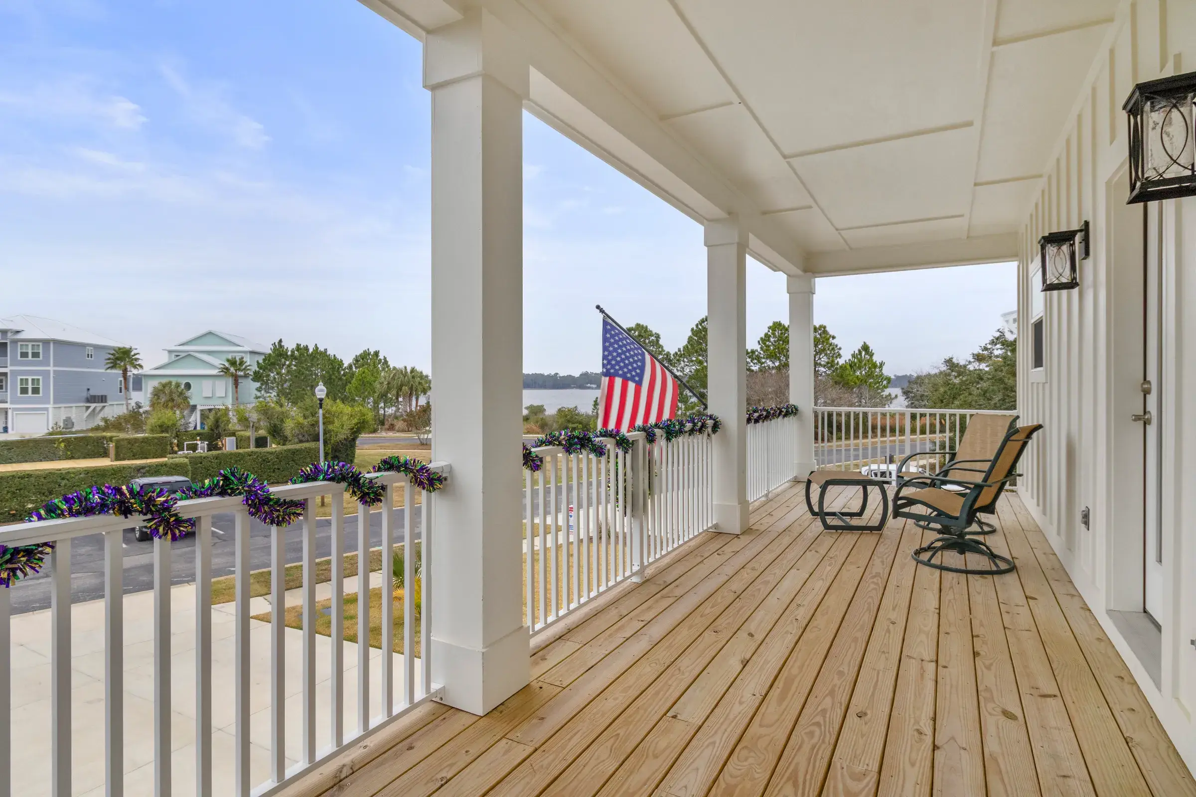 Wide wood front porch with white railings, rocking chairs and an American flag overlooking the water.