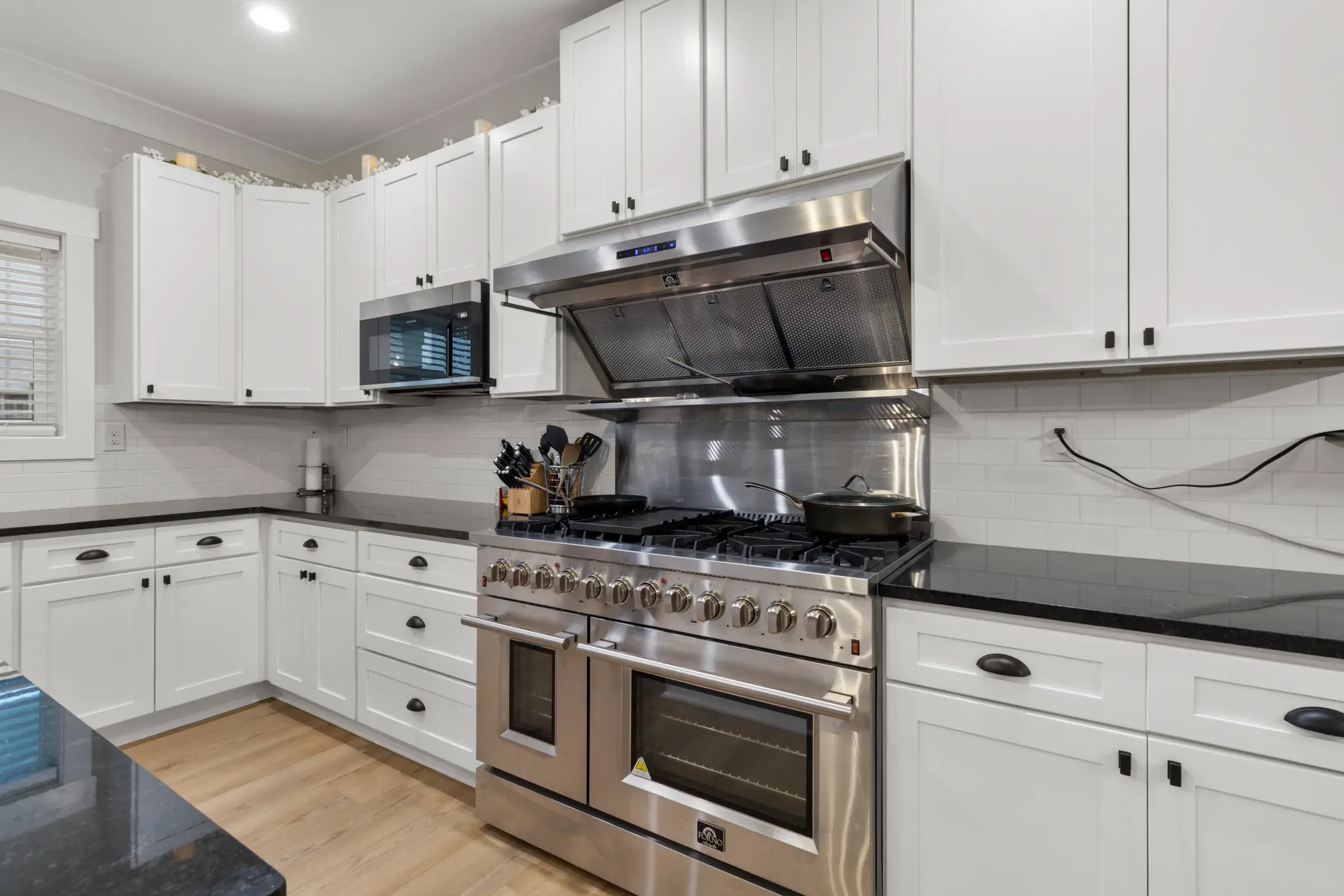 Stainless gas range with double ovens under a hood, flanked by white cabinets and dark granite counters.