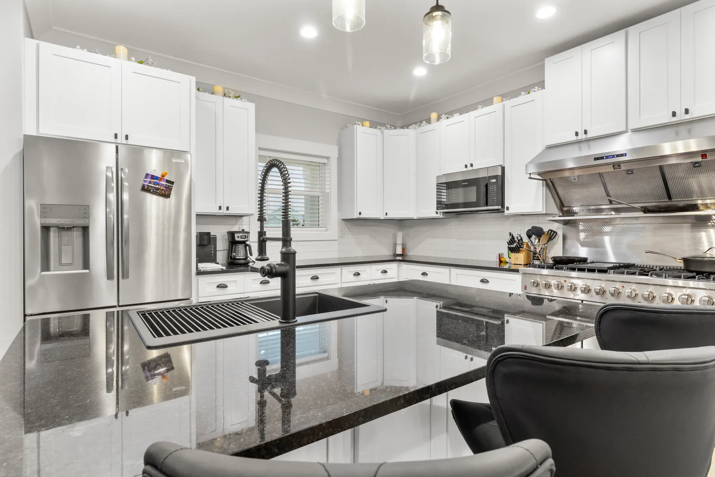 Dark granite island with sink and faucet, white cabinets, stainless refrigerator and gas range behind.