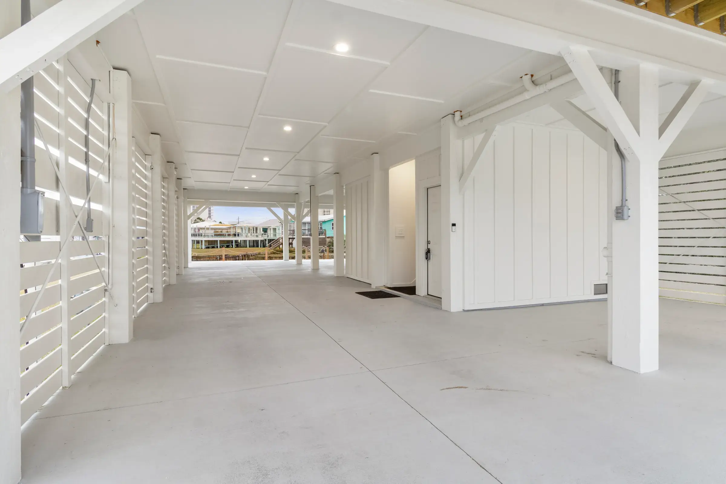Open concrete ground-level parking area with white slatted screens, columns and a view of the water at the far end.