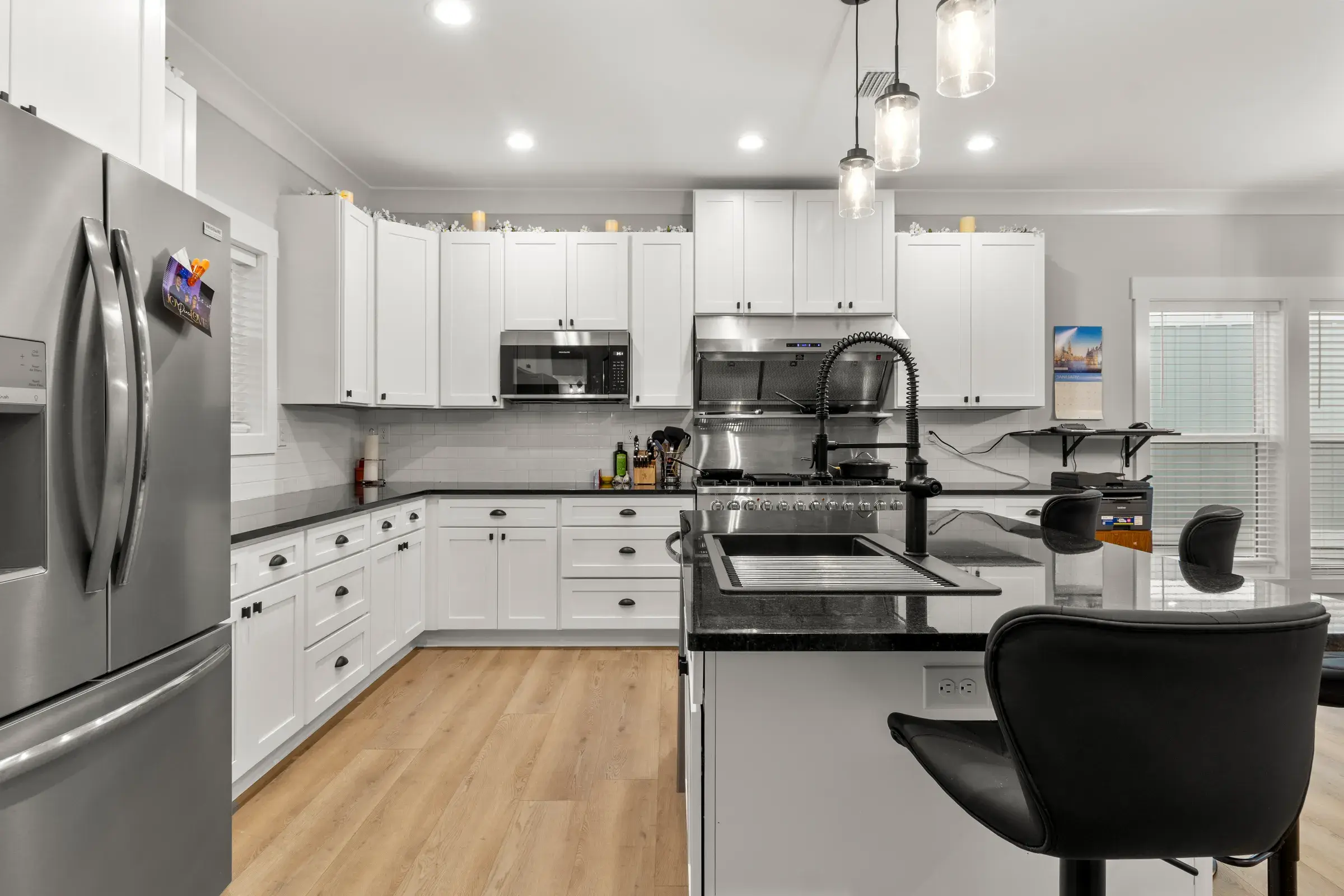 White shaker cabinets, stainless refrigerator and a dark granite island with a black faucet and workstation sink.