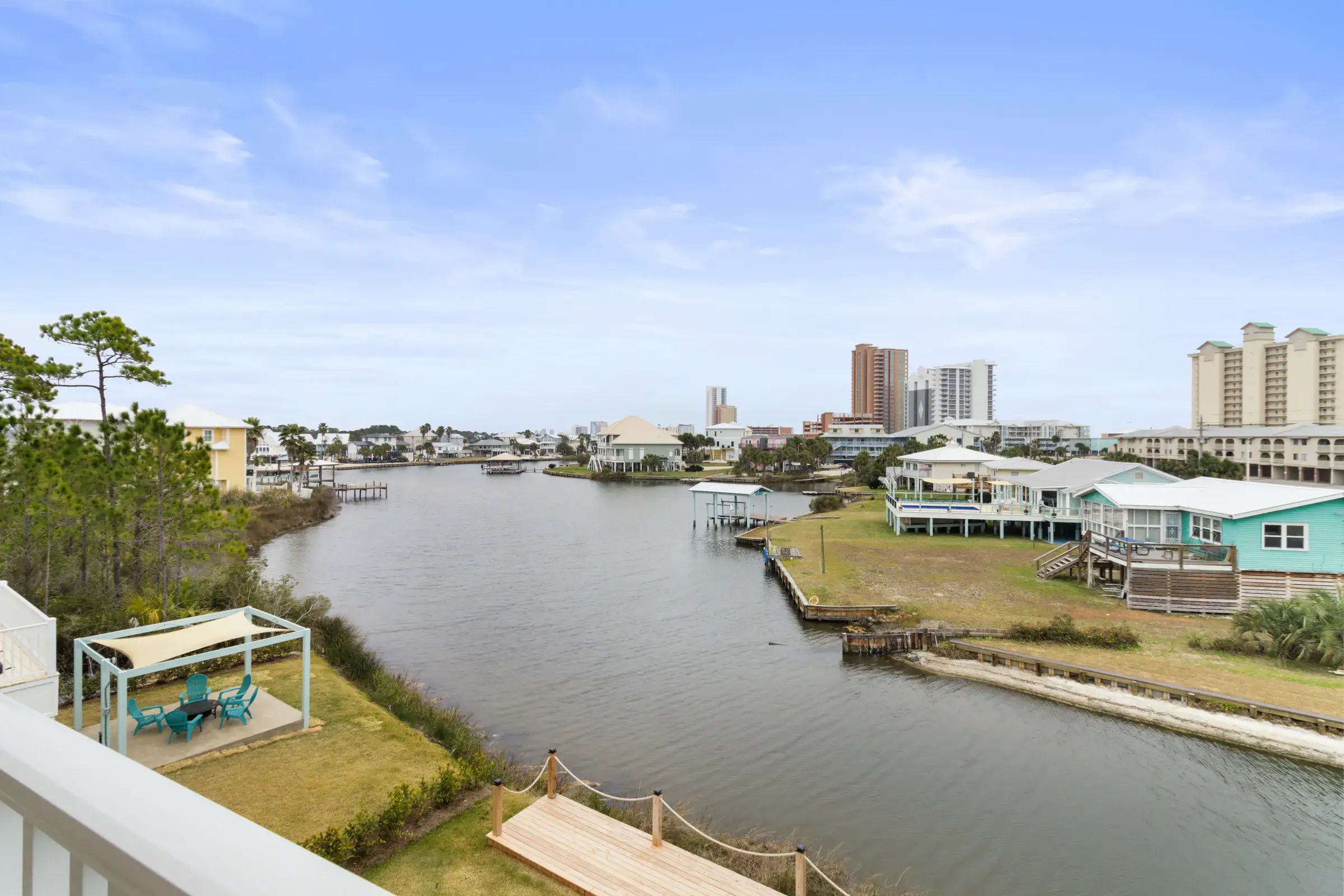 Elevated view of the lagoon with a wooden dock, a seating area, neighboring homes, and condo towers beyond.