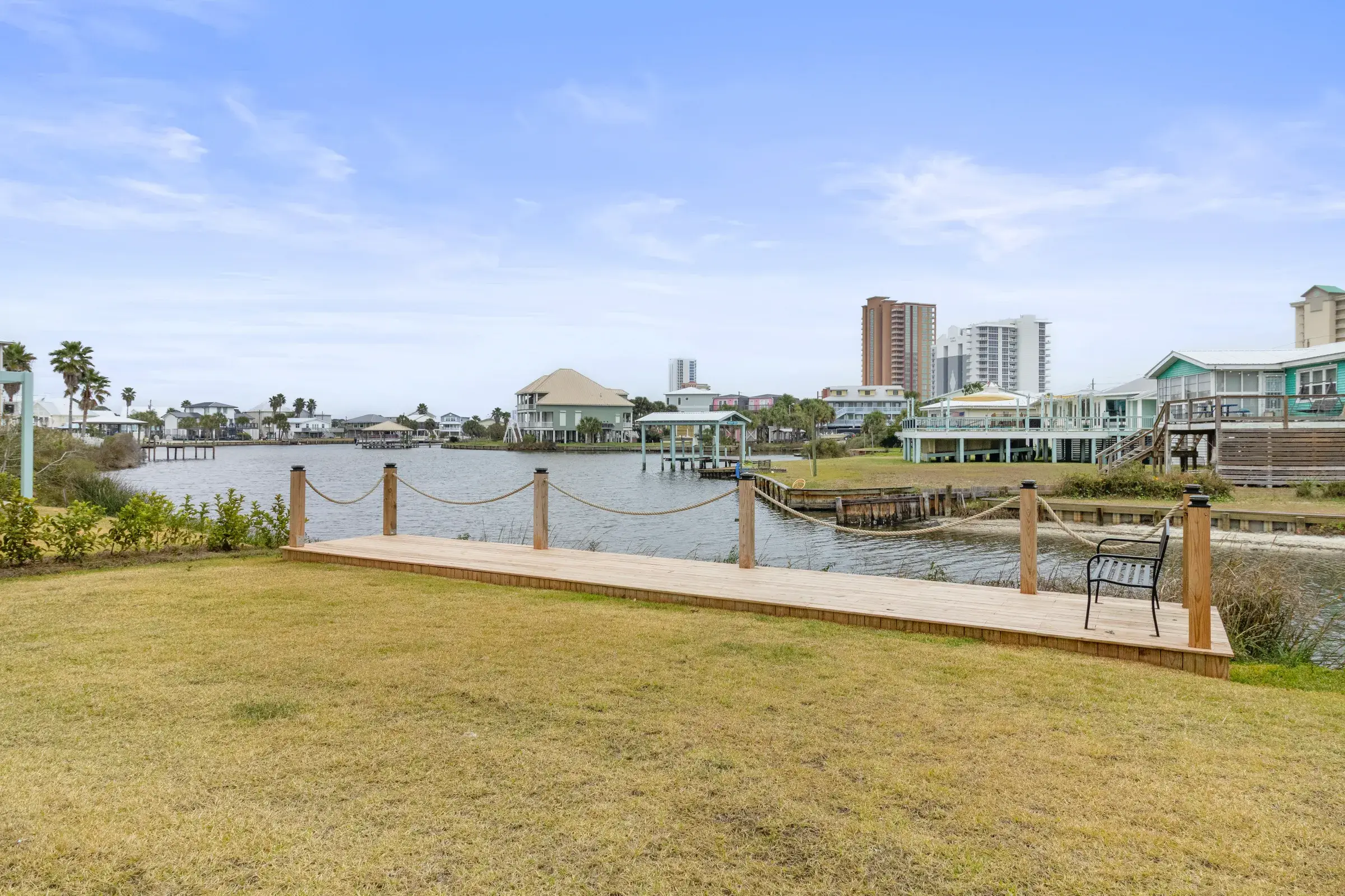 Wooden boardwalk with rope railing and a bench along the lagoon, with a lawn in front.
