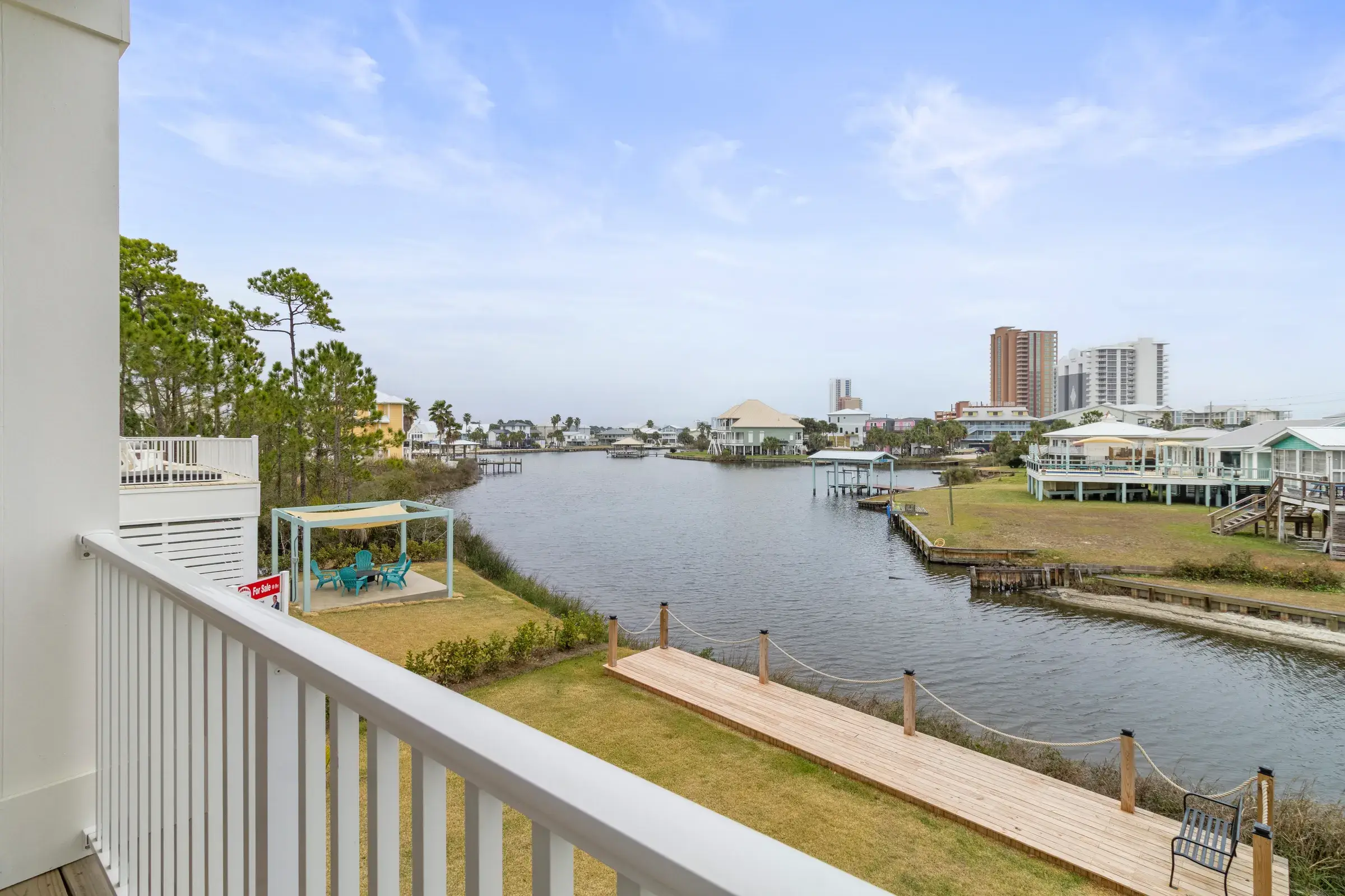 View from the deck railing across the lagoon, with a wooden boardwalk and bench on the lawn below.