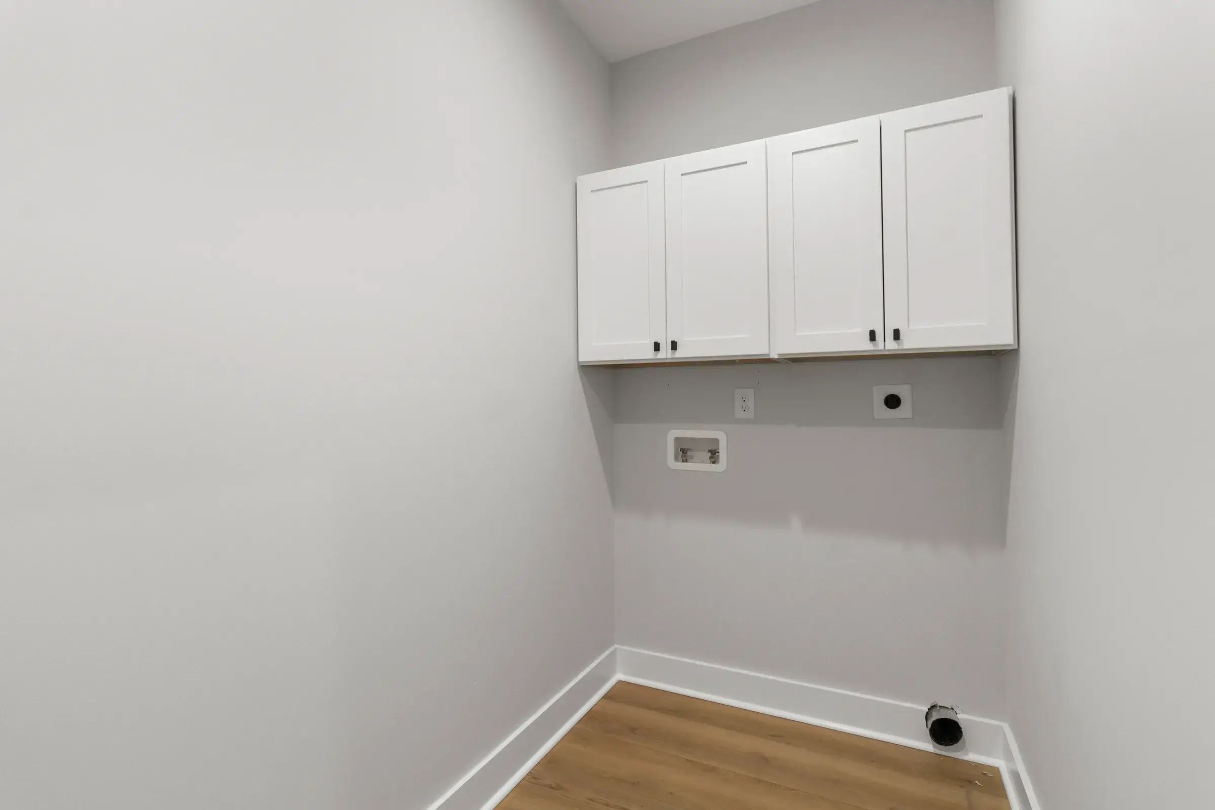 Laundry room with white upper cabinets, washer hookup box, and wood-look flooring.
