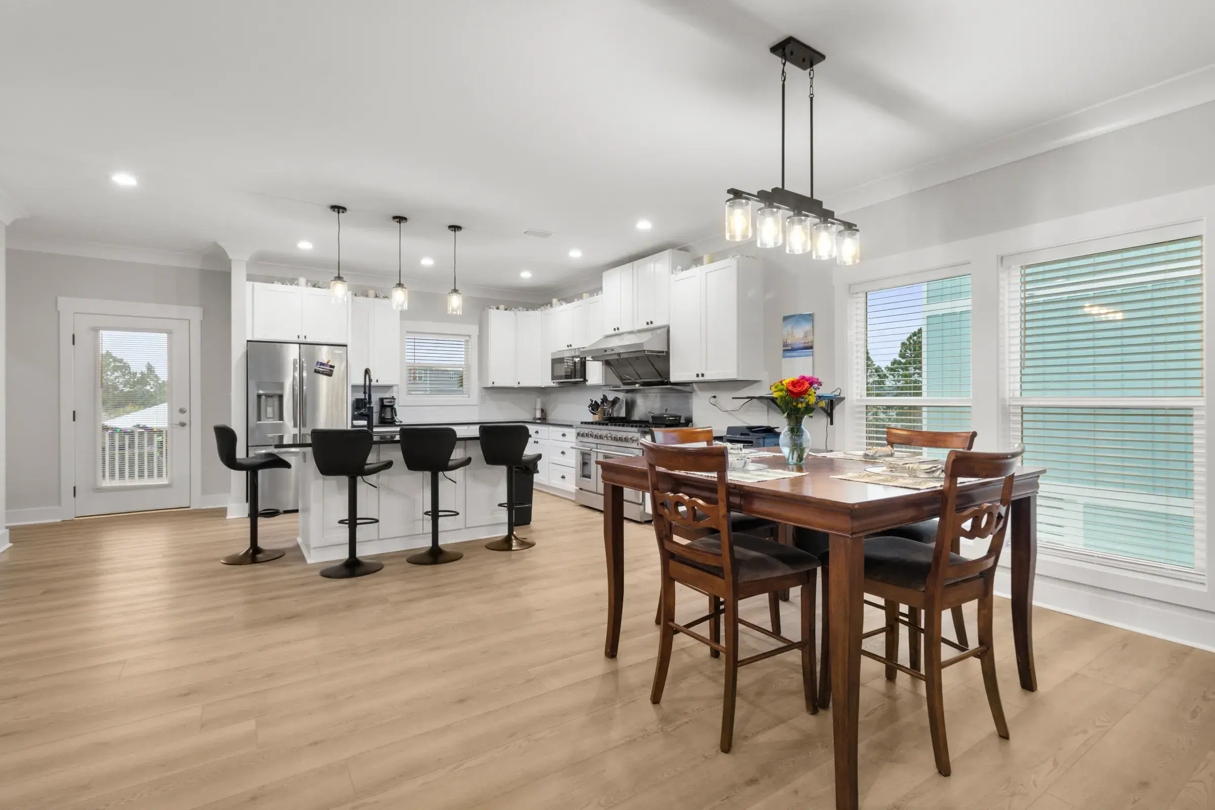 Open kitchen with island and black barstools beside a wood dining table under pendant lights.