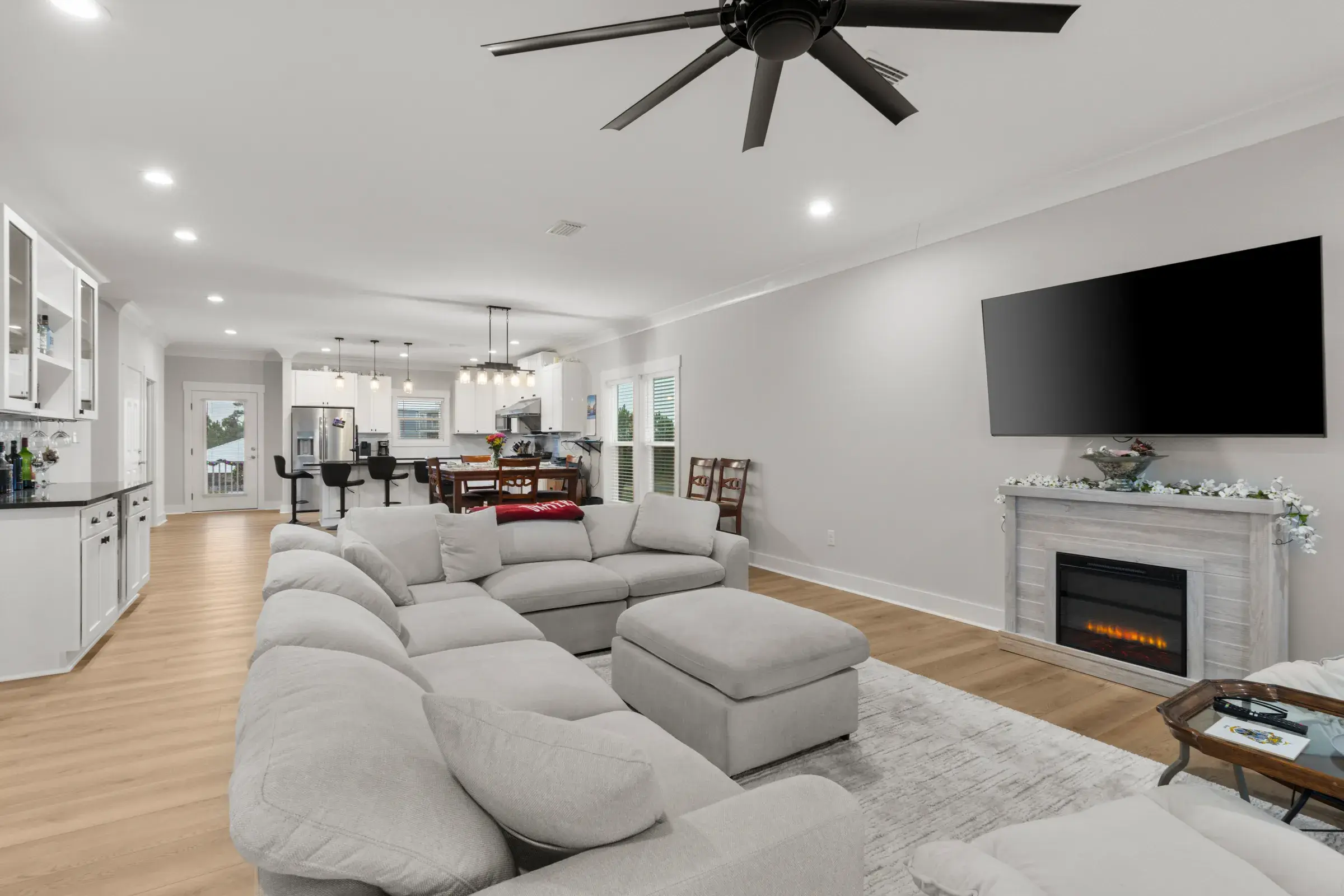 Open-plan living area with a sectional, fireplace and TV, with the dining area and kitchen in the background.