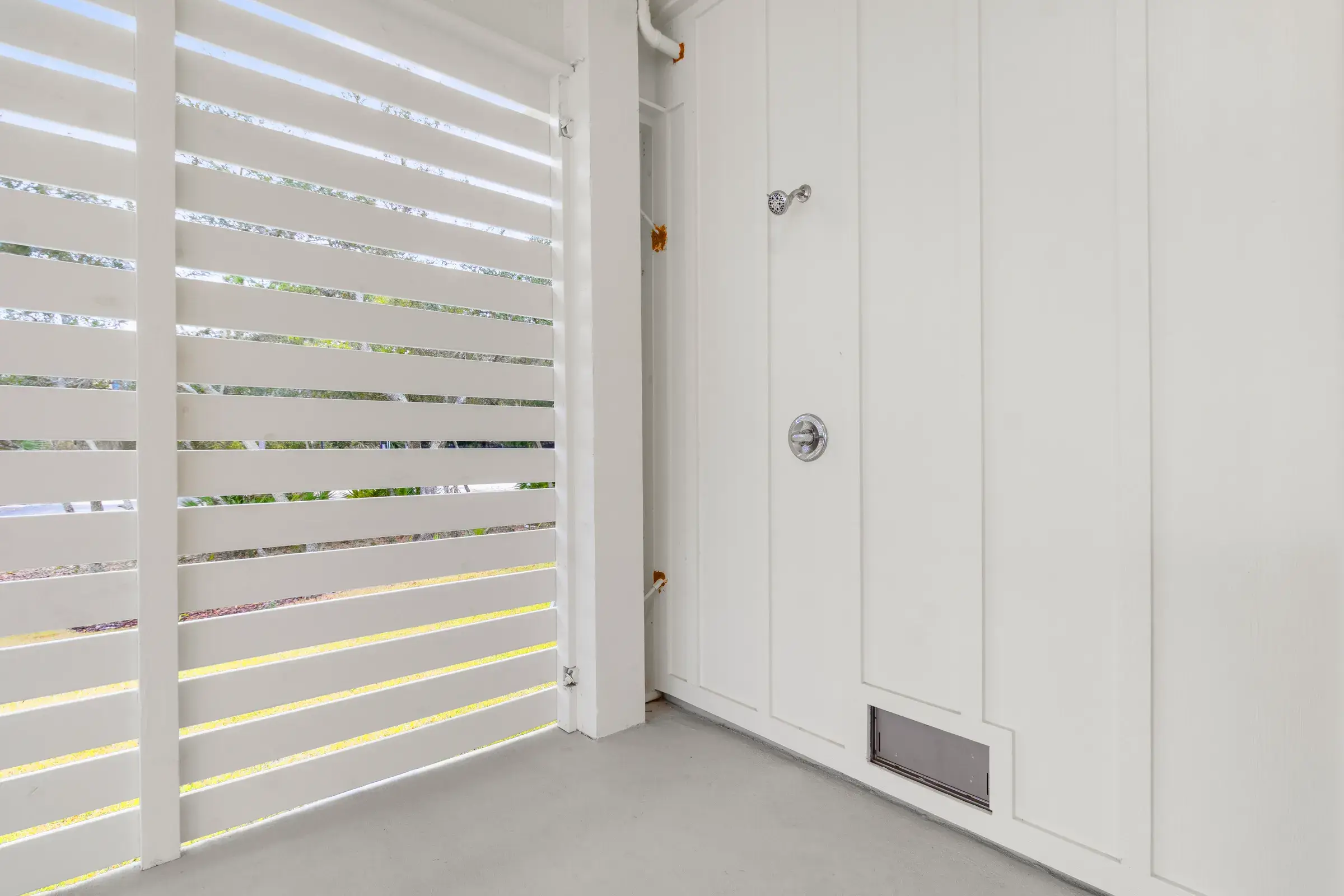 Corner of the ground level with a slatted privacy screen and a wall-mounted shower valve.