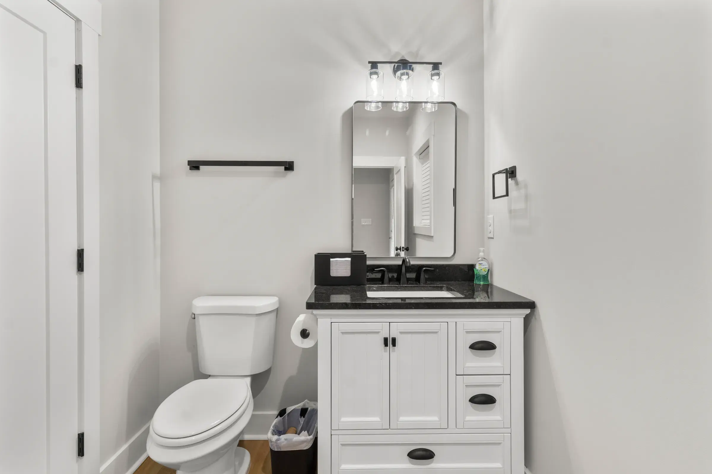 Half bath with white vanity, dark granite top, framed mirror and vanity light.