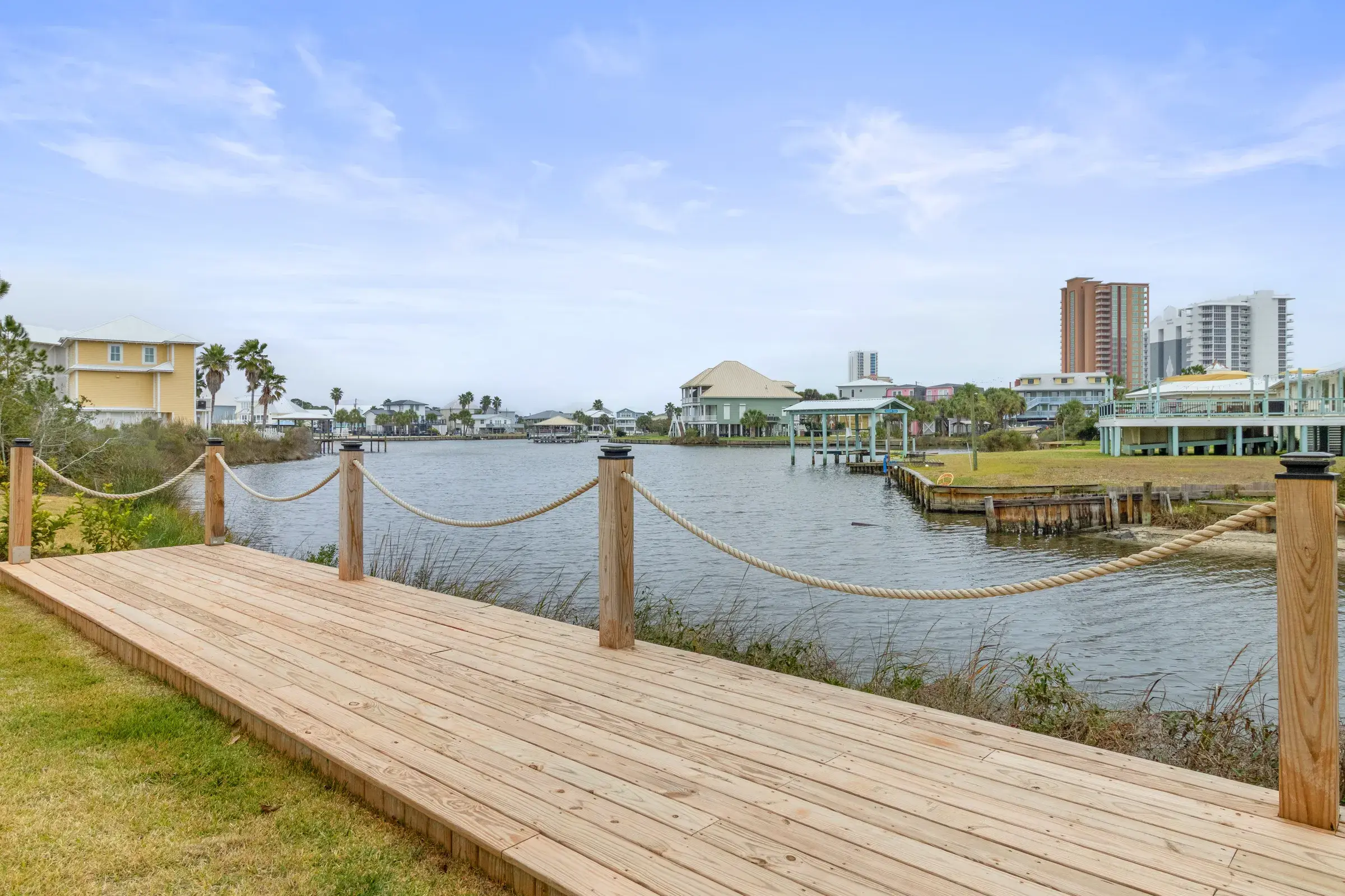 Wooden boardwalk with rope railing beside the lagoon and distant waterfront homes.