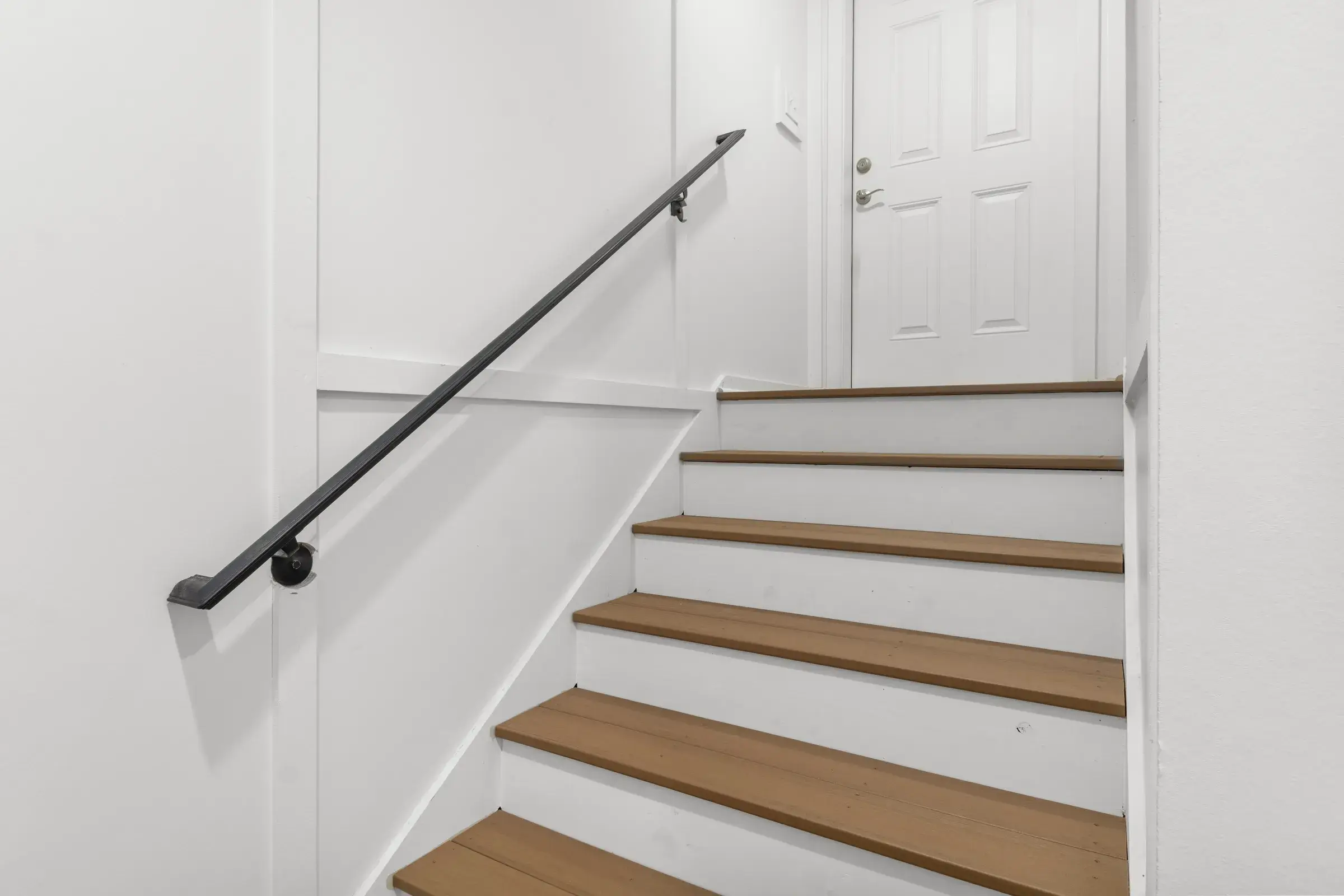 White stairwell with wood-toned treads and a black metal handrail.