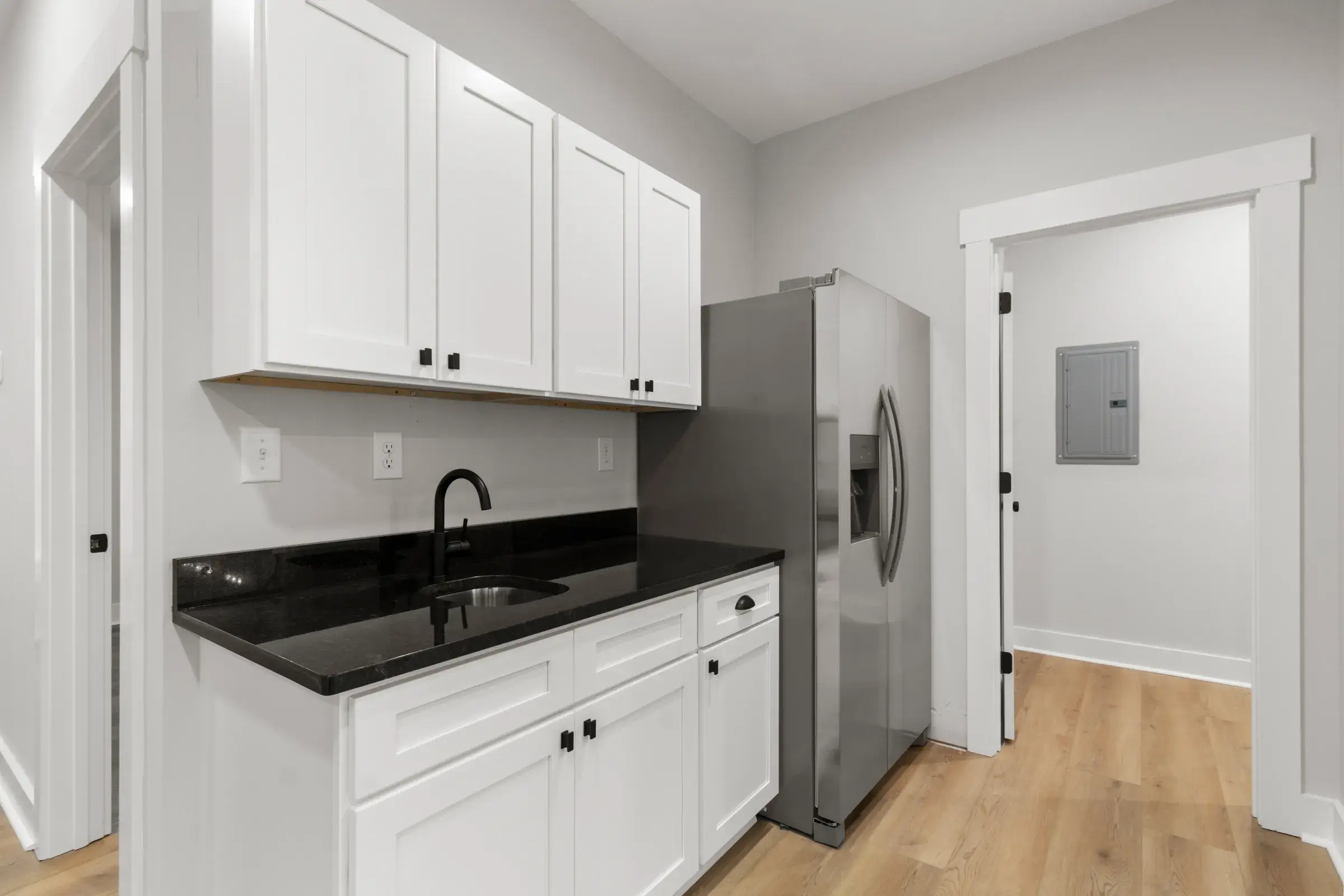 Kitchenette with white shaker cabinets, dark granite counter and sink, and a stainless refrigerator.
