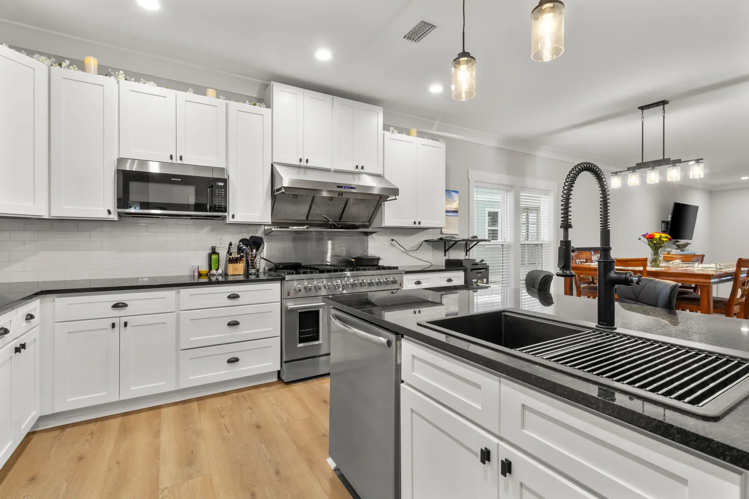 Black gooseneck faucet and workstation sink in a dark granite island, with the range and dining area behind.